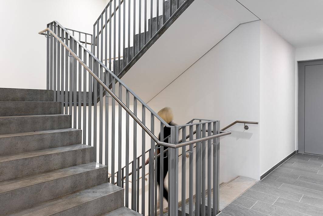 Modernes Treppenhaus mit robusten Steinstufen und eleganten Metallgeländern, eine Person steigt die Treppe hinauf.