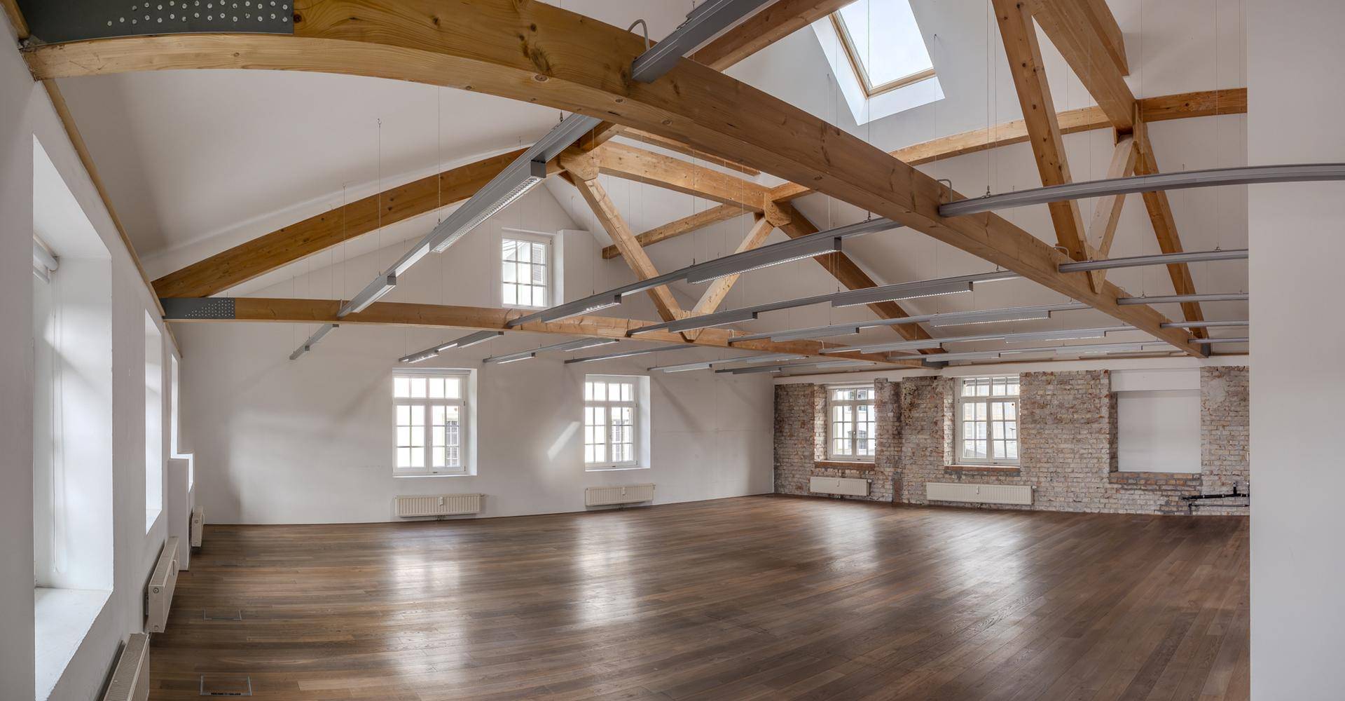 Geräumiger Loftbereich mit Holzboden, freiliegenden Dachbalken und einer Kombination aus weißen Wänden und unverputztem Mauerwerk.
