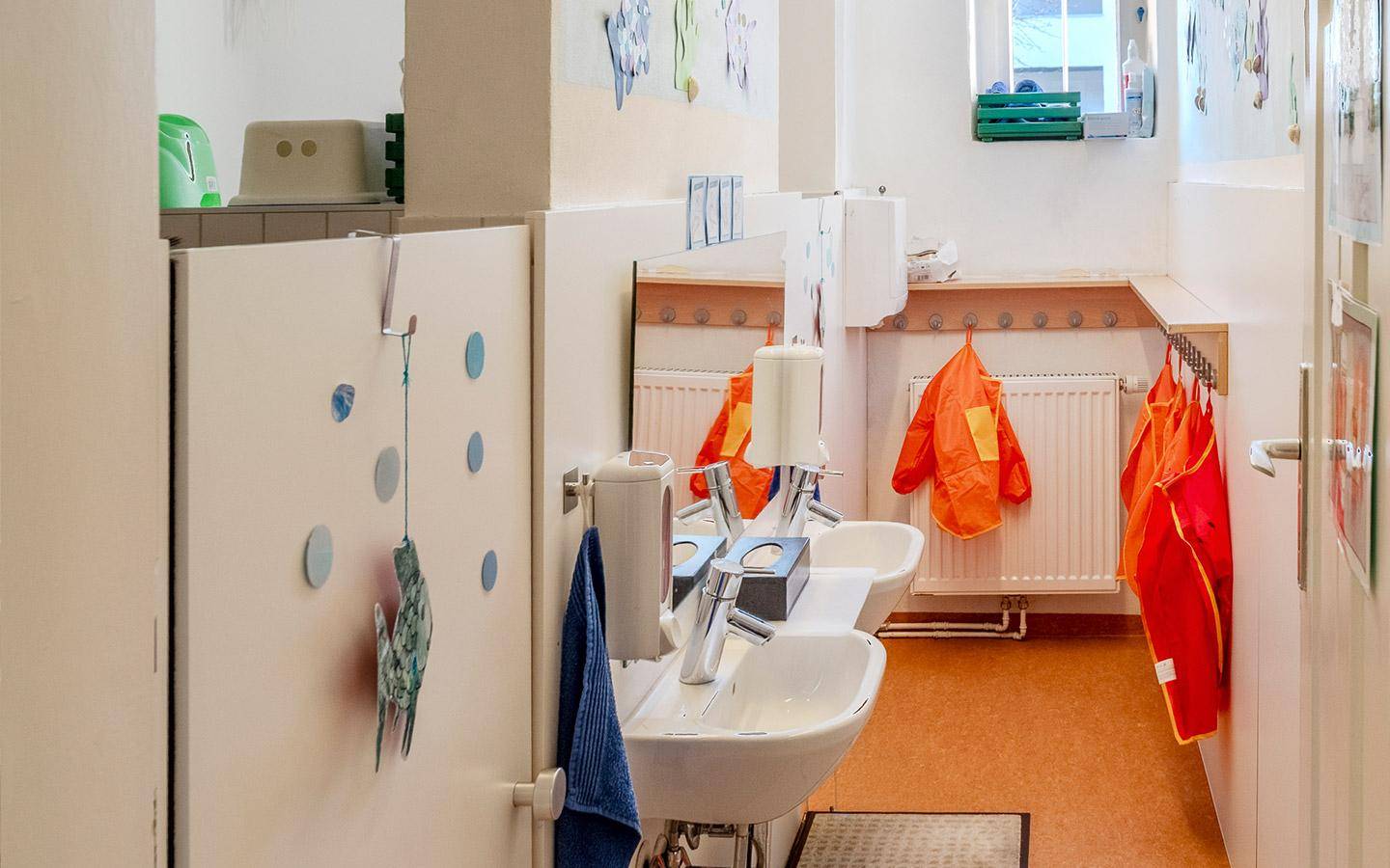Kinderfreundliches Badezimmer mit niedrigen Waschbecken und bunten Handtüchern, hell und funktional.