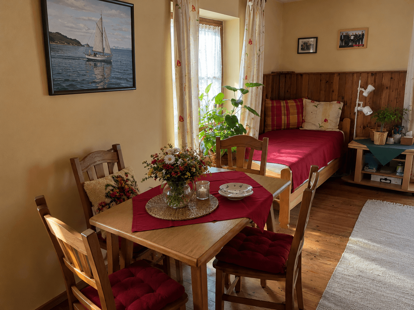 Gemütliches Schlafzimmer mit Holzbett, kleinem Esstisch und natürlichem Lichteinfall durch das Fenster.