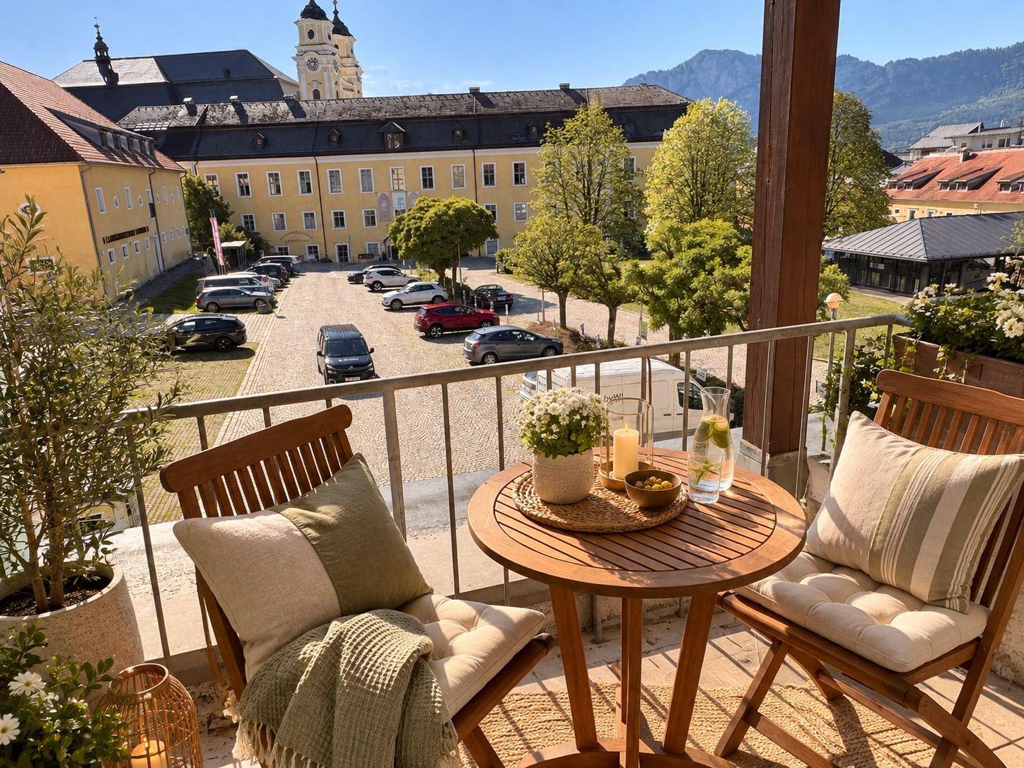 Möblierter Balkon mit Holztisch und Stühlen, bietet einen weiten Blick auf die Stadt und Berge.