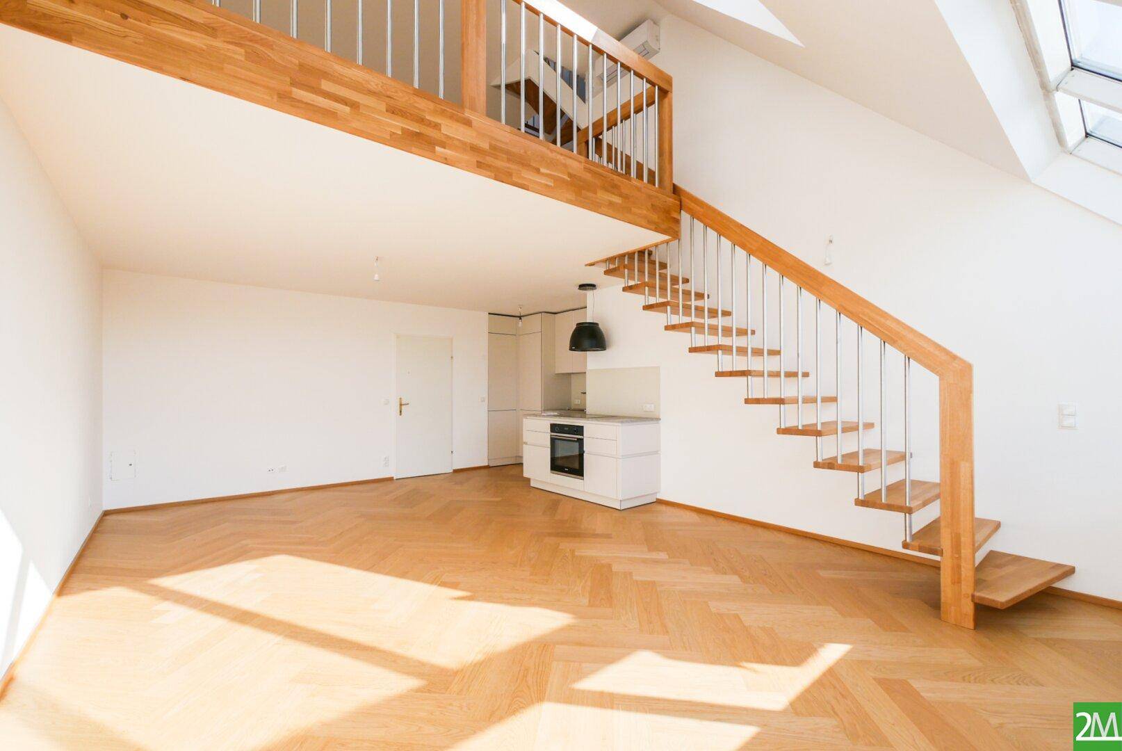 Geräumiger Wohnbereich mit Holzparkett, offener Treppe und einer Galerie, lichtdurchflutet durch Dachfenster.