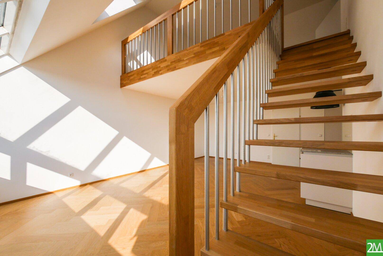 Detailansicht der Holztreppe mit Metallgeländer, die zu einer Galerie in einem hellen Raum führt.