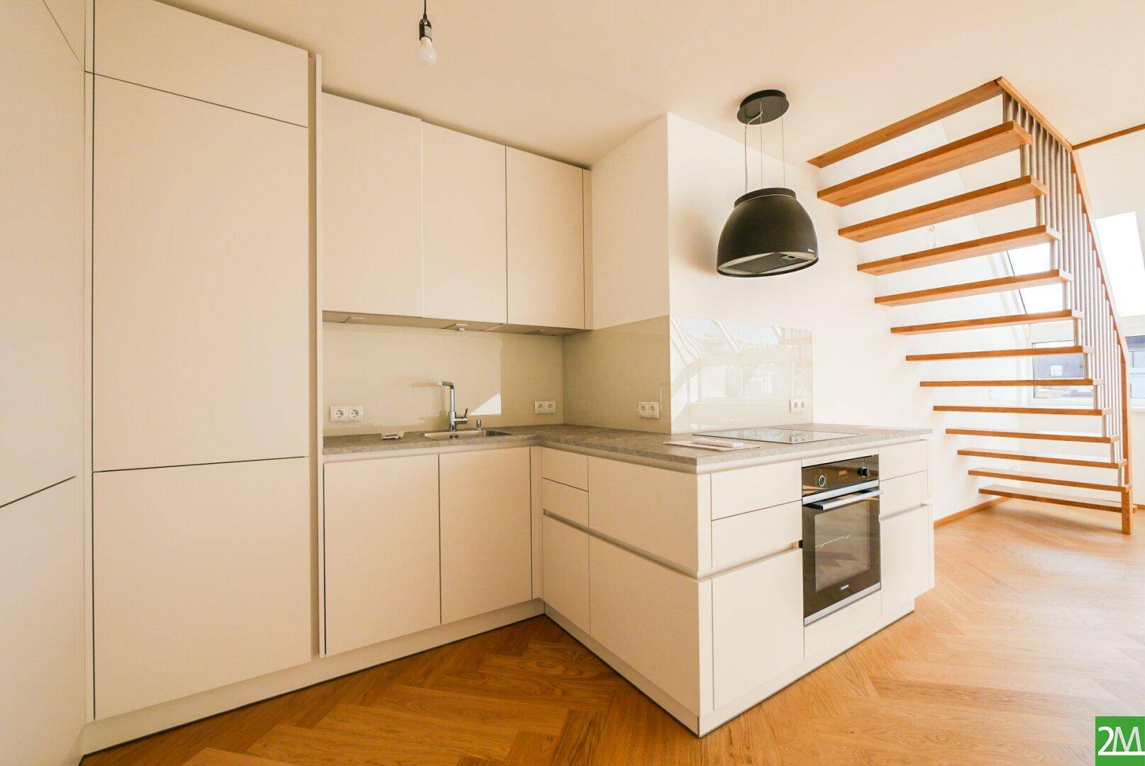 Detailansicht einer modernen, hellen Einbauküche mit integriertem Backofen und Holzparkettboden.