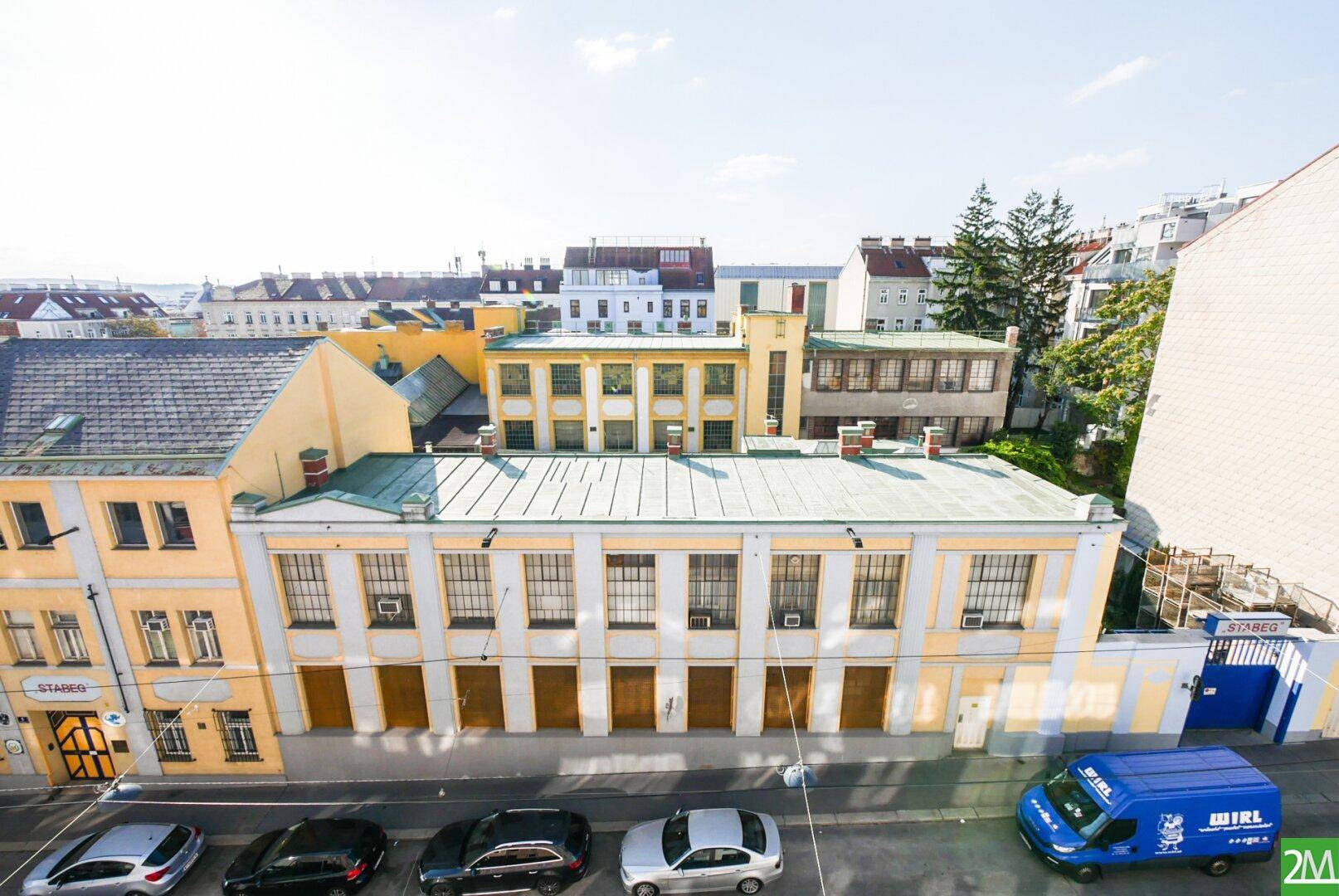 Blick auf eine städtische Straße mit Gebäuden und parkenden Autos unter blauem Himmel.