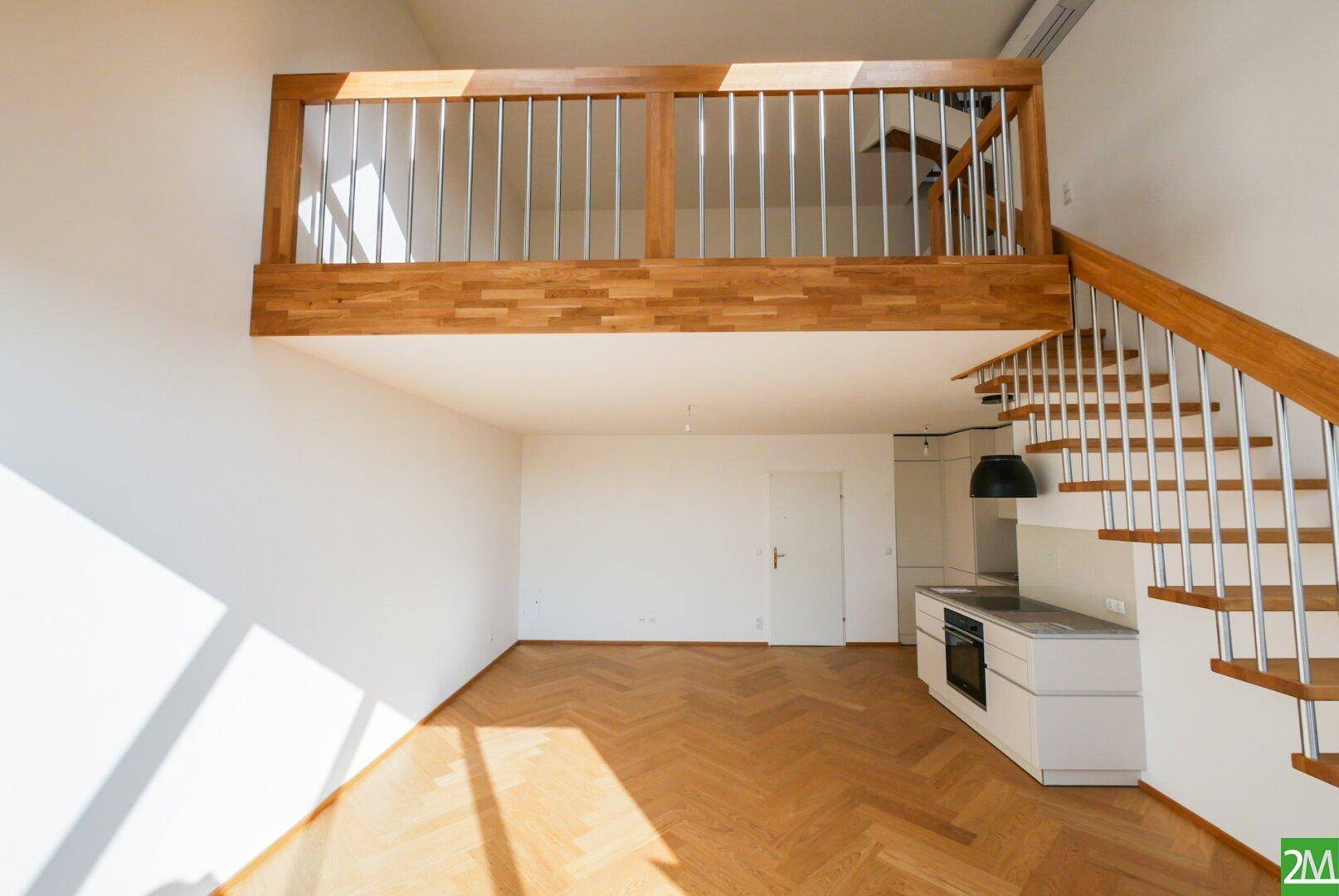 Heller Wohnbereich mit Holzparkett, offener Treppe und Galerie, die den Raum vertikal erweitert.