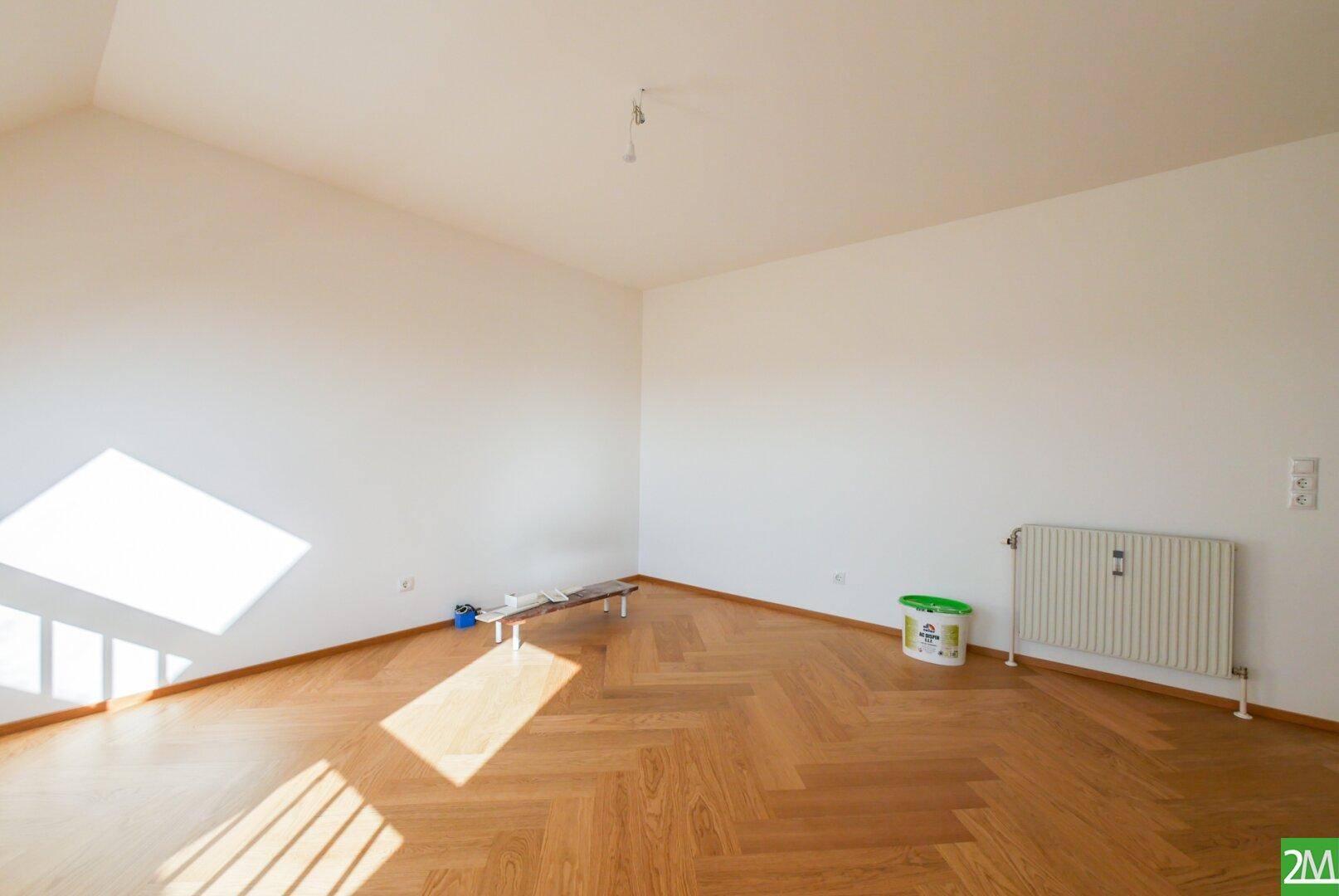 Leerer, heller Raum mit Holzparkettboden und einem Heizkörper, bereit zur individuellen Gestaltung.