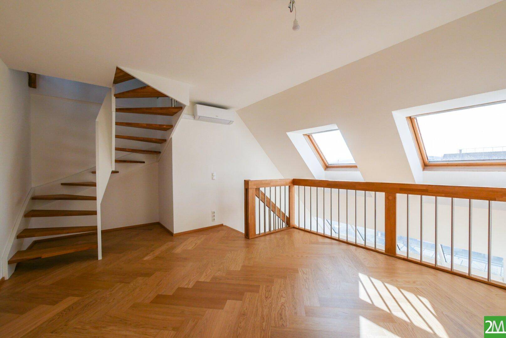Heller Wohnbereich im Dachgeschoss mit Holzparkett, Galerie und Dachfenstern, die den Raum erhellen.