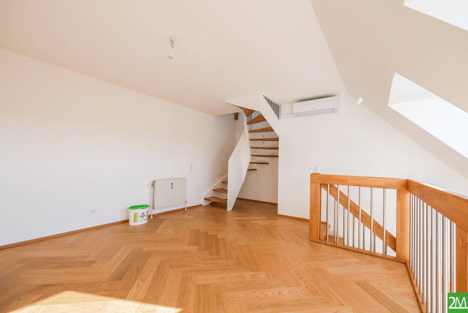 Geräumiger Dachgeschoss-Wohnbereich mit Holzparkett, offener Treppe und Klimaanlage.