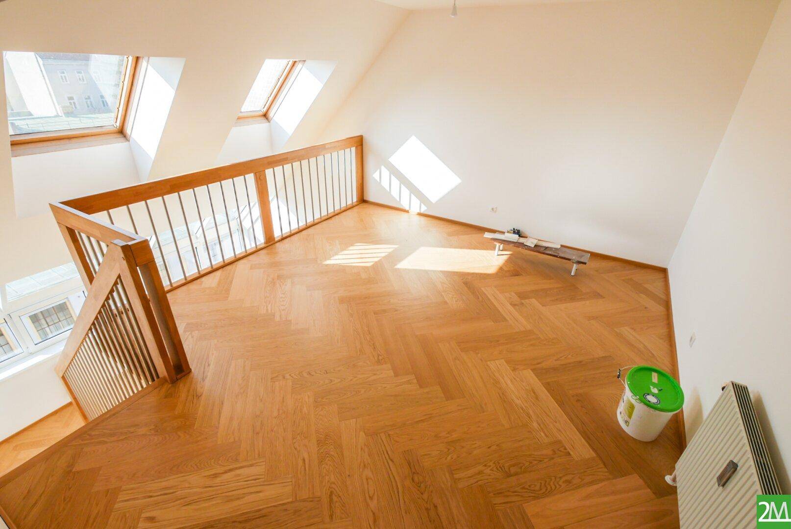 Heller Dachgeschossraum mit Holzparkett, Galerie und Dachfenstern, die den Raum mit Licht füllen.