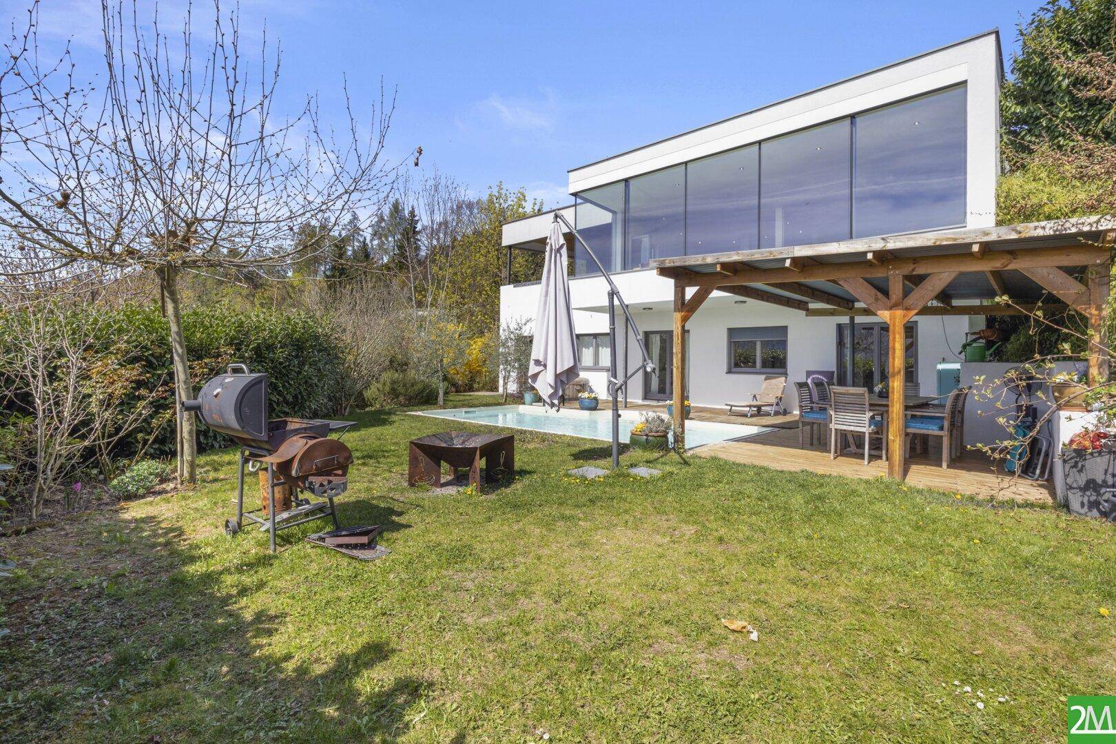 Gepflegter Garten mit Rasenfläche, Grillbereich und Blick auf das moderne Haus mit Pool.