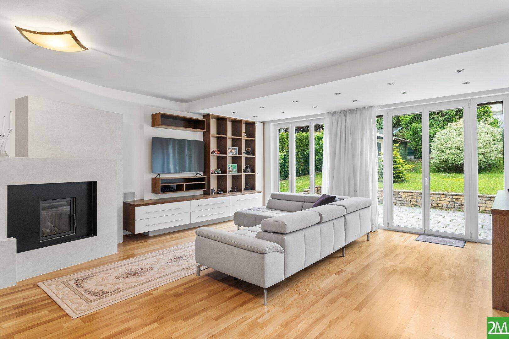 Helles Wohnzimmer mit modernem Kamin, großem Sofa und Zugang zur grünen Gartenterrasse.