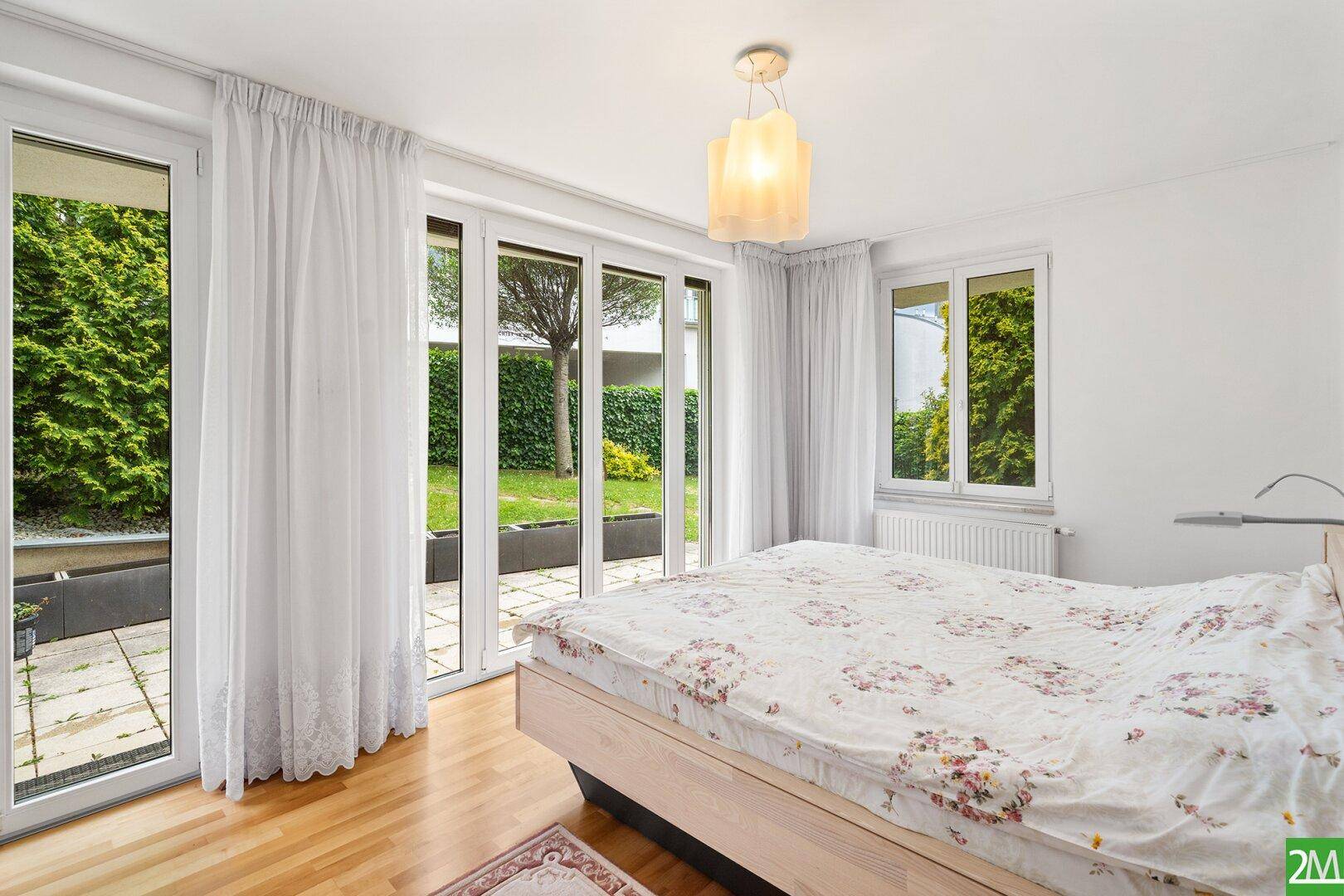Schlafzimmer mit Holzboden, großem Bett und direktem Zugang zu einer privaten Terrasse im Garten.