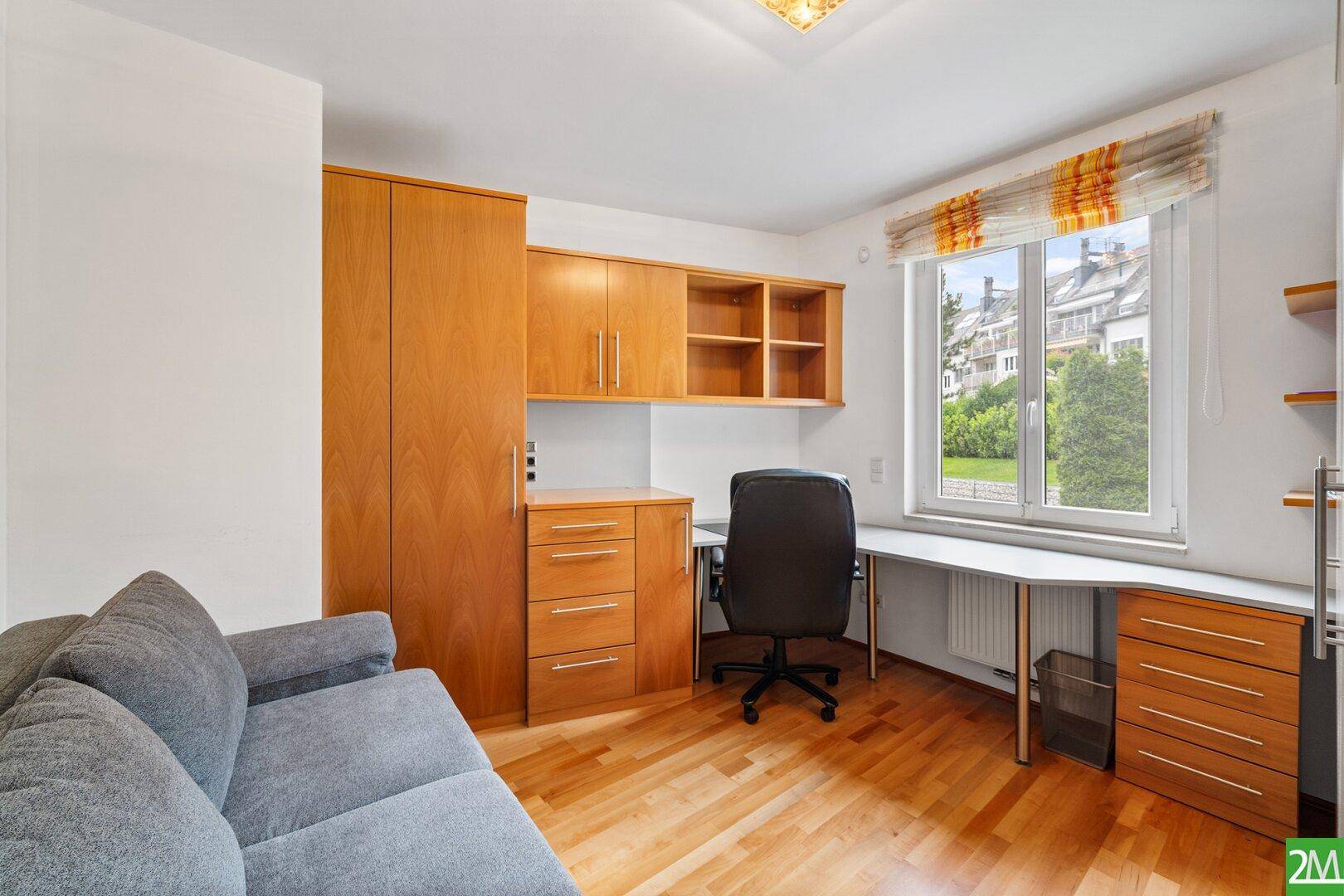 Helles Arbeitszimmer mit Holzboden, Einbauschränken und einem Fenster mit Blick auf die Umgebung.