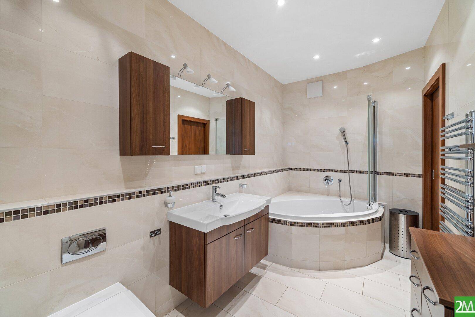 Modernes Badezimmer mit beigen Fliesen, Eckbadewanne mit Dusche und beheiztem Handtuchhalter.