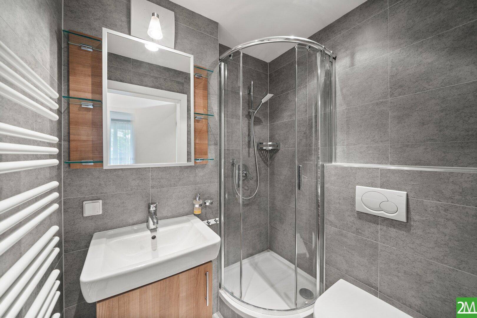 Kleines Badezimmer mit grauen Fliesen, Duschkabine und modernem Waschbecken.