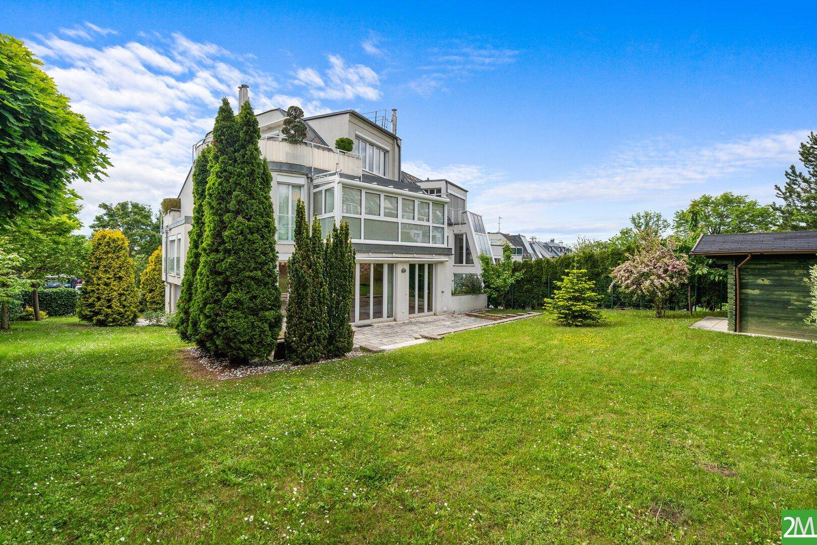 Weitläufiger Garten mit Rasenfläche, Terrasse und modernem Haus im Hintergrund.
