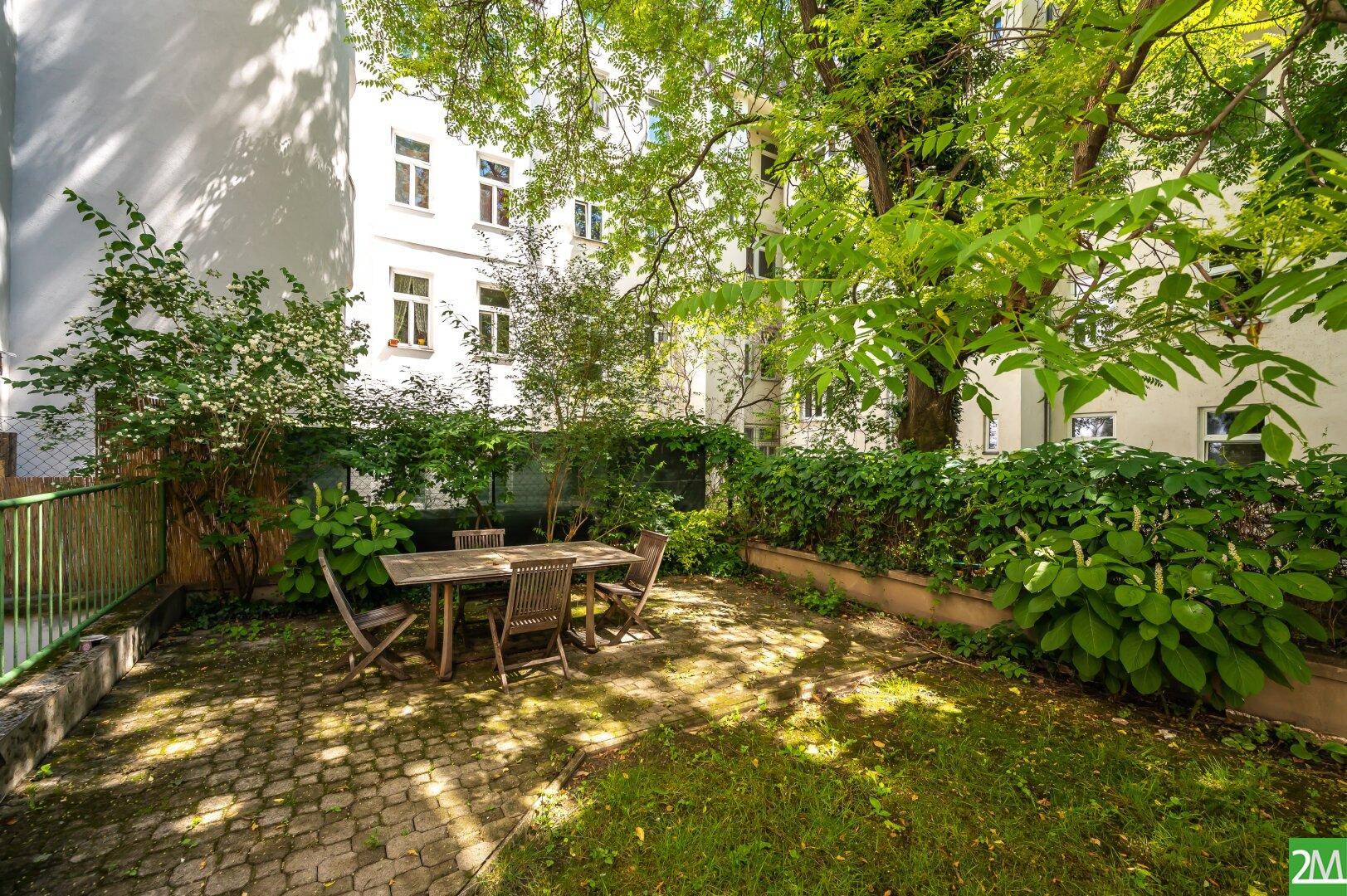 Grüner Innenhofgarten mit Sitzgelegenheiten und viel Baumbestand, umgeben von Wohngebäuden.