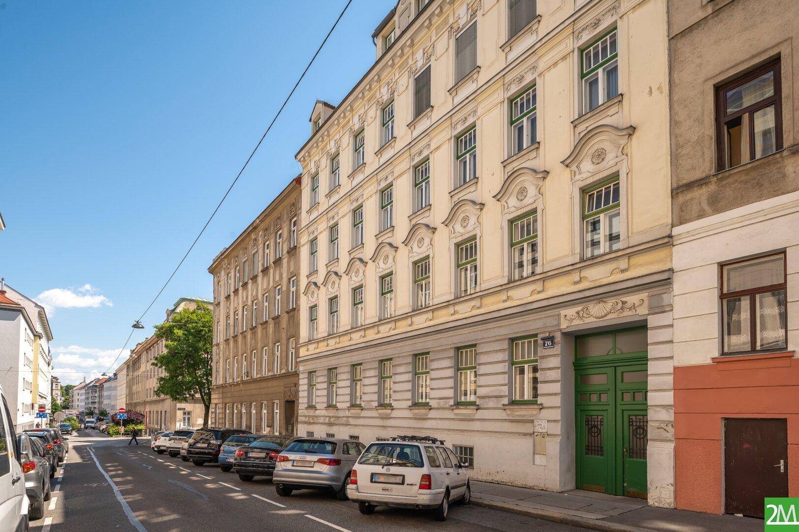 Historische Fassade eines Mehrfamilienhauses an einer belebten Straße mit parkenden Autos.