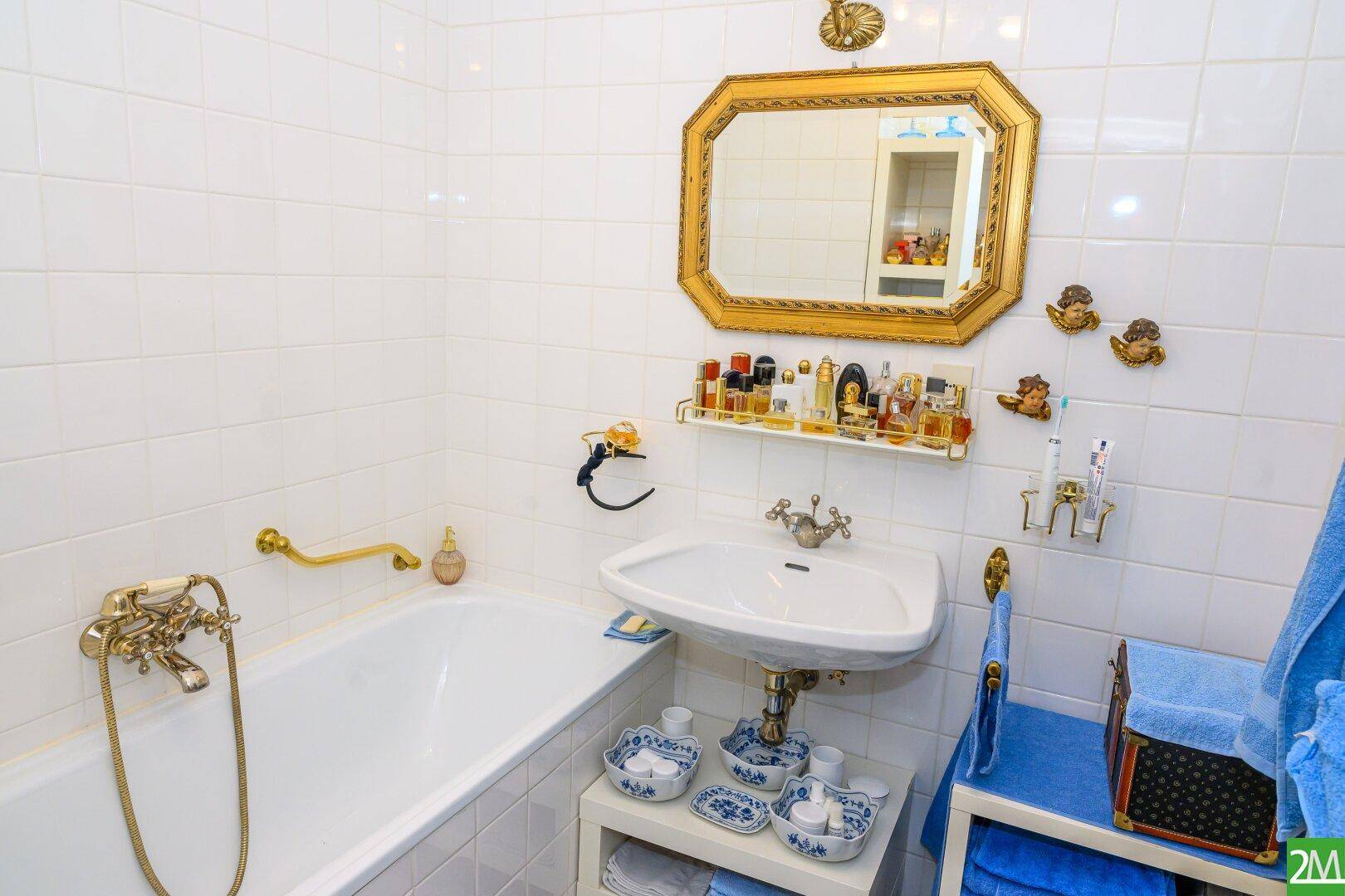 Helles Badezimmer mit Badewanne, Waschbecken und einem goldenen Spiegel, komplett gefliest.