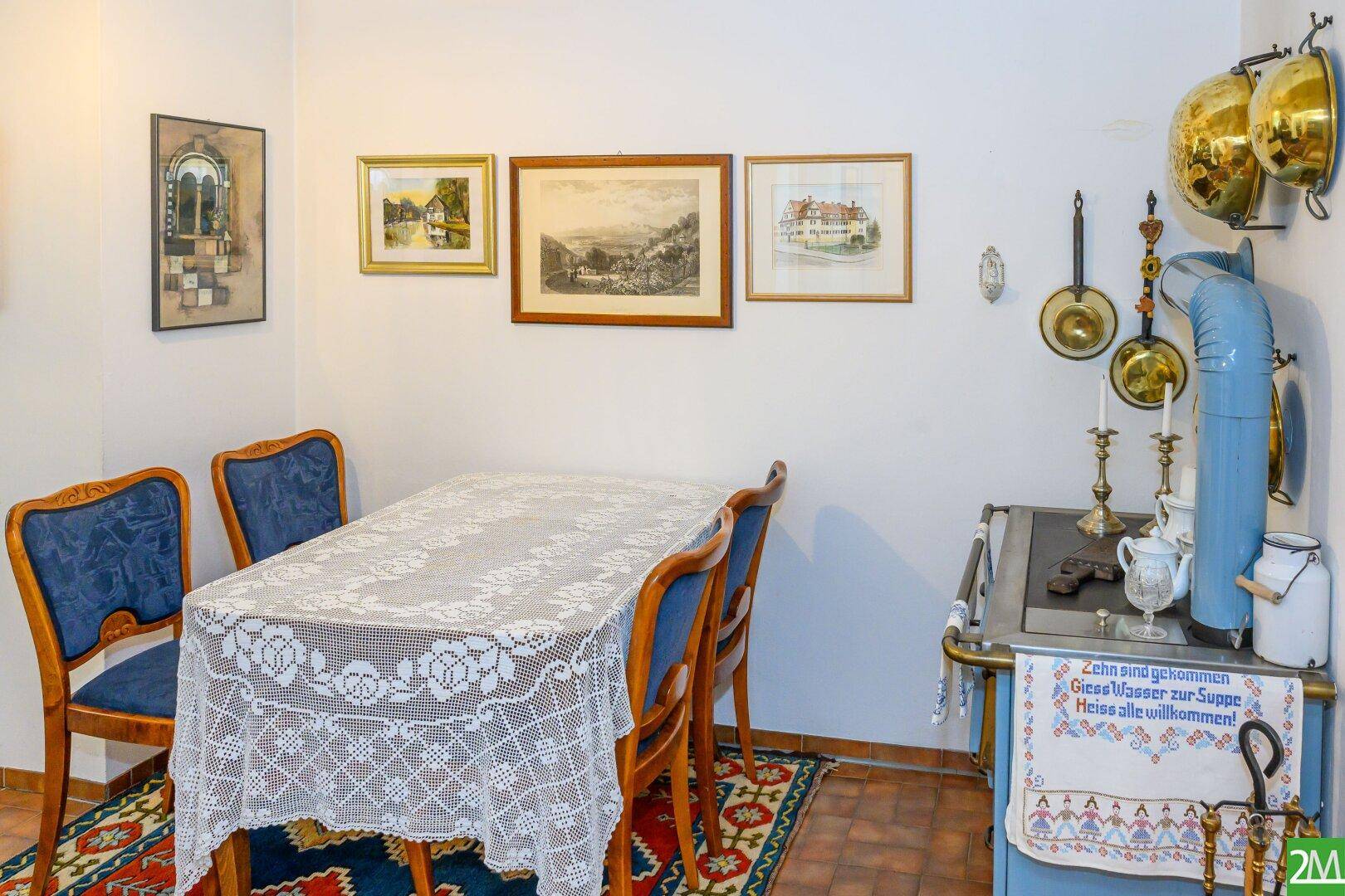 Gemütlicher Essbereich mit traditionellem Holztisch, blauen Stühlen und einem dekorativen Ofen.