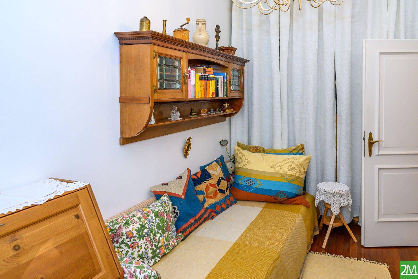 Helles Schlafzimmer mit Einzelbett, Holzregal und farbenfrohen Kissen, ideal als Gästezimmer.