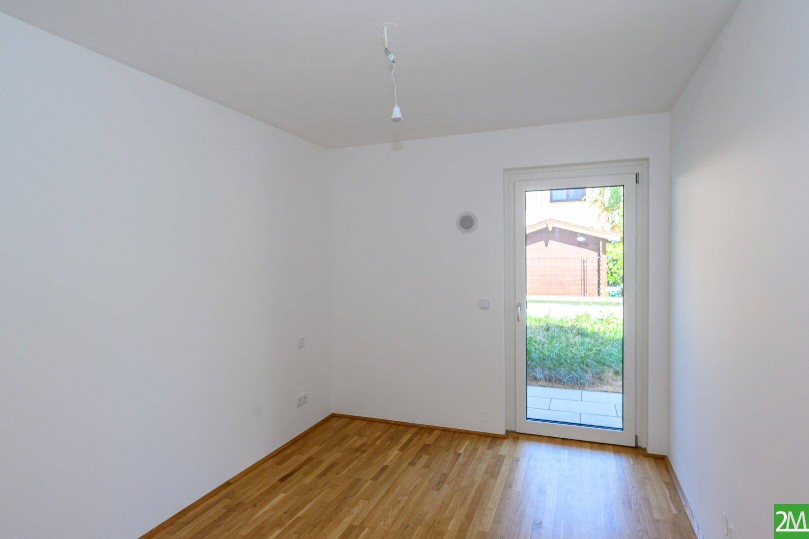 Leeres Zimmer mit Holzboden und Zugang zu einem kleinen Außenbereich.