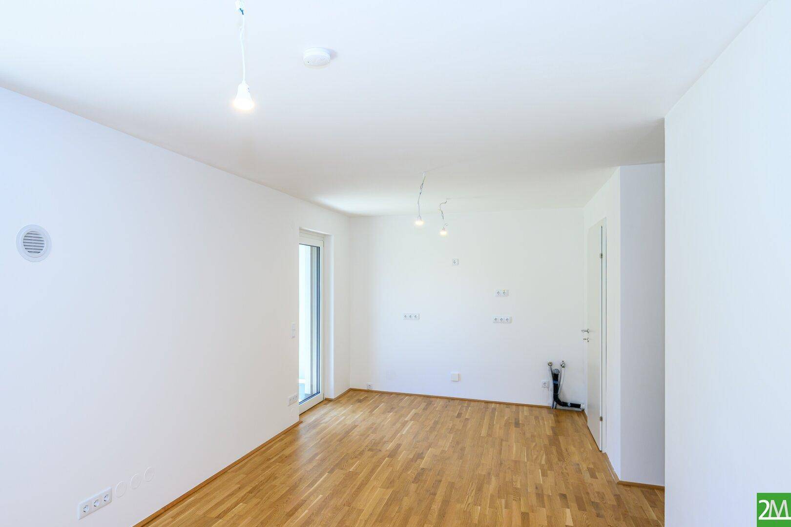 Heller Raum mit Holzboden und Anschlüssen für eine zukünftige Küche.