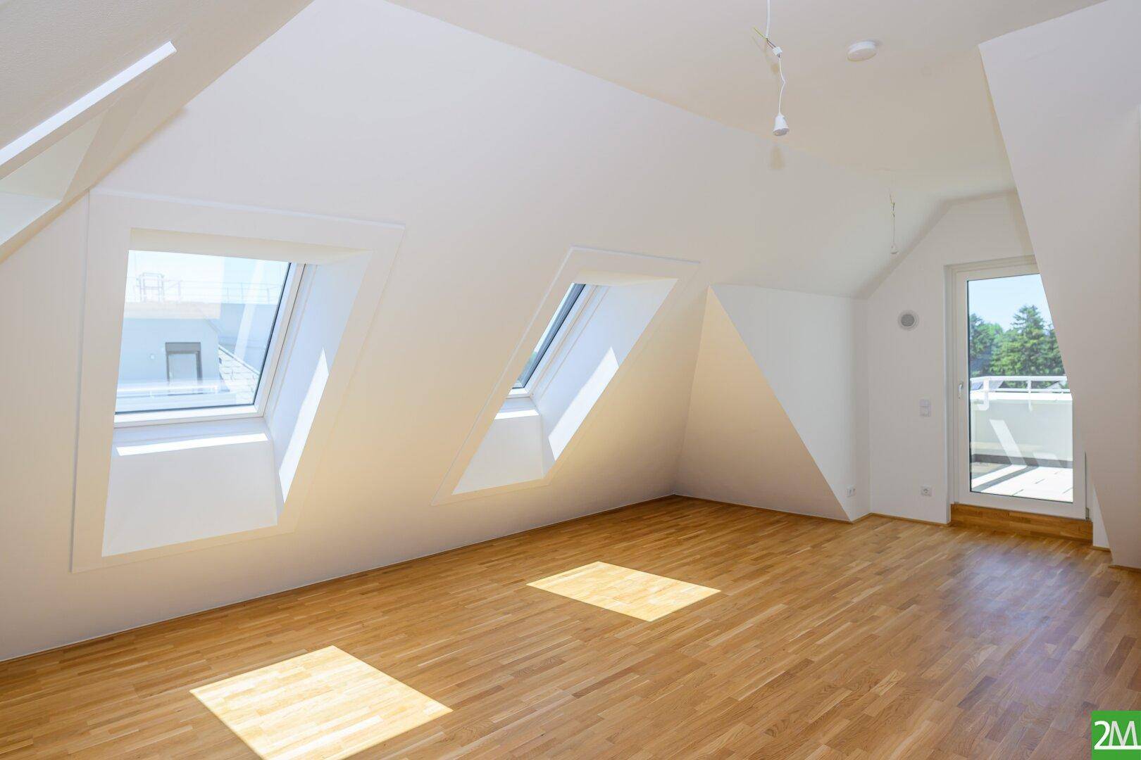 Heller Raum im Dachgeschoss mit Holzboden und mehreren Dachfenstern, die viel Licht hereinlassen.
