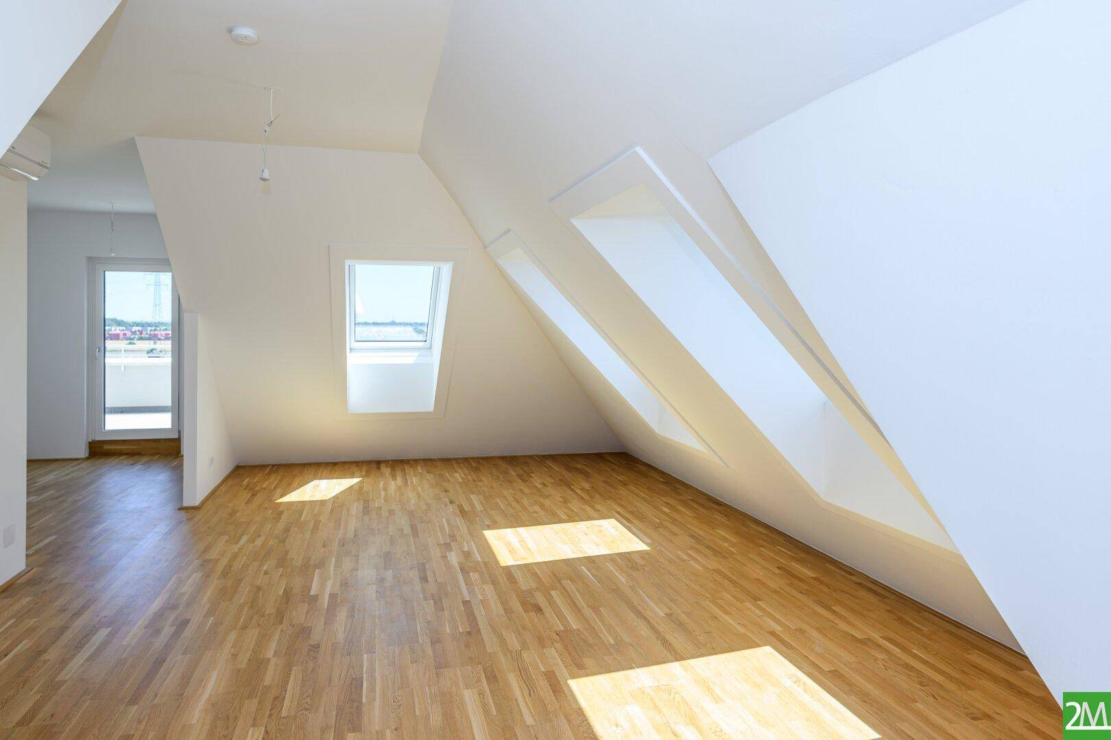 Lichtdurchfluteter Dachgeschossraum mit Holzboden und schrägen Wänden, ausgestattet mit Dachfenstern.