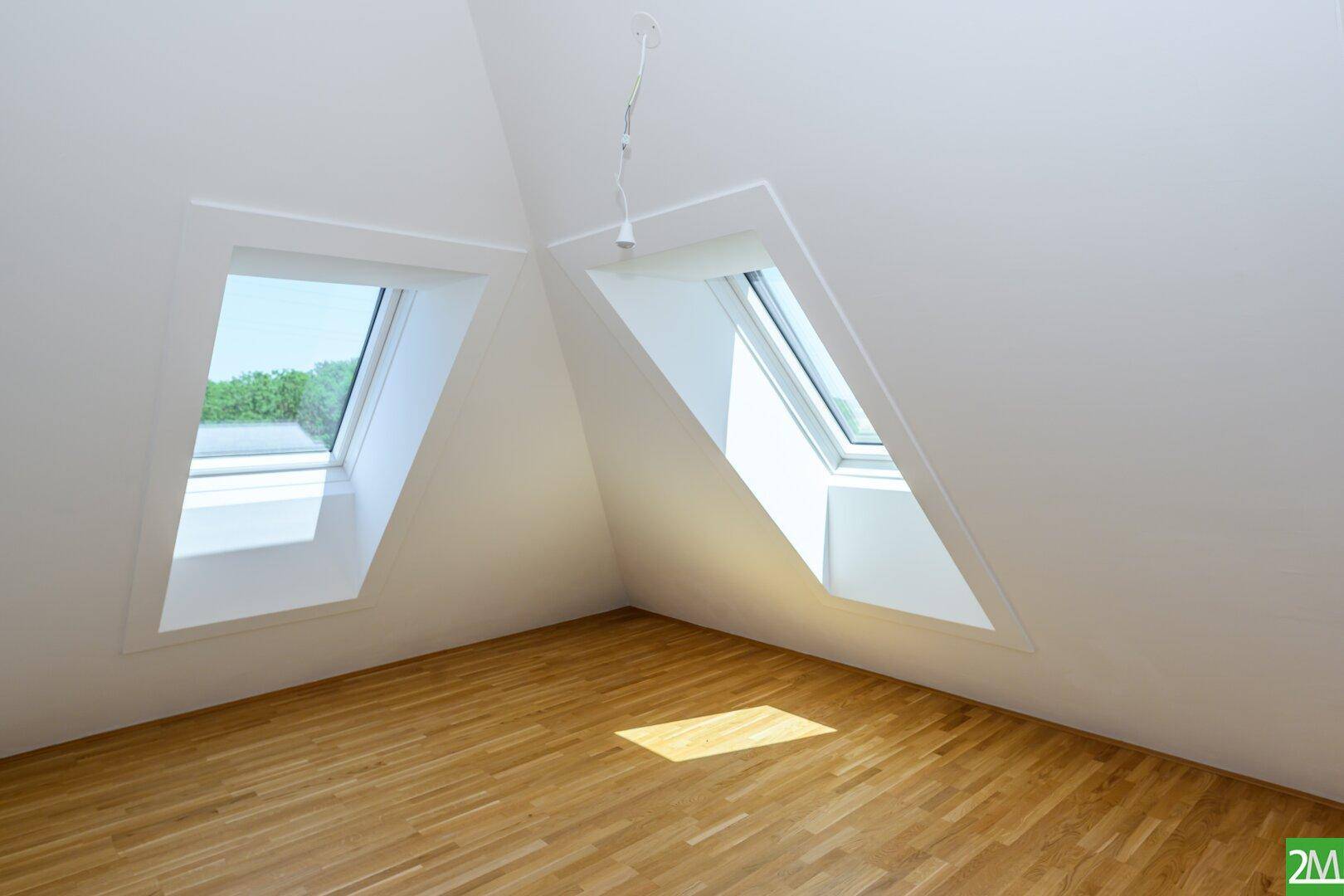 Geräumiger Dachgeschossraum mit Holzboden und zwei großen Dachfenstern für viel Tageslicht.