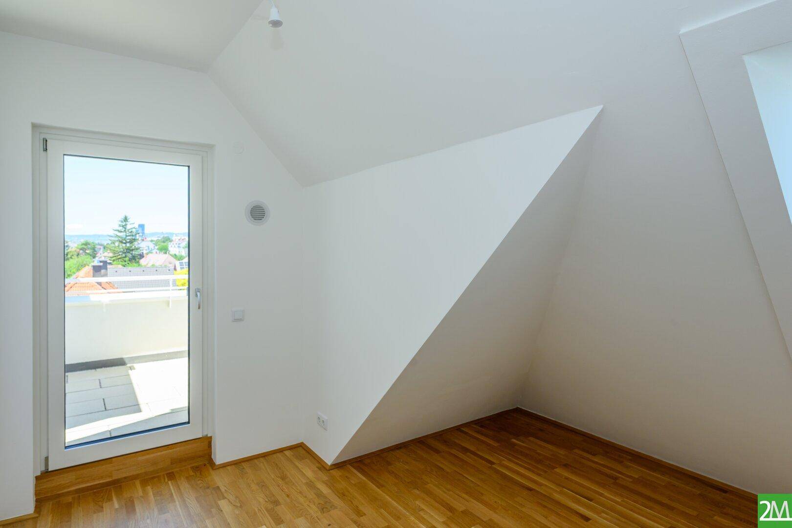 Dachgeschossraum mit Holzboden und Zugang zu einem Balkon, der eine weite Aussicht bietet.
