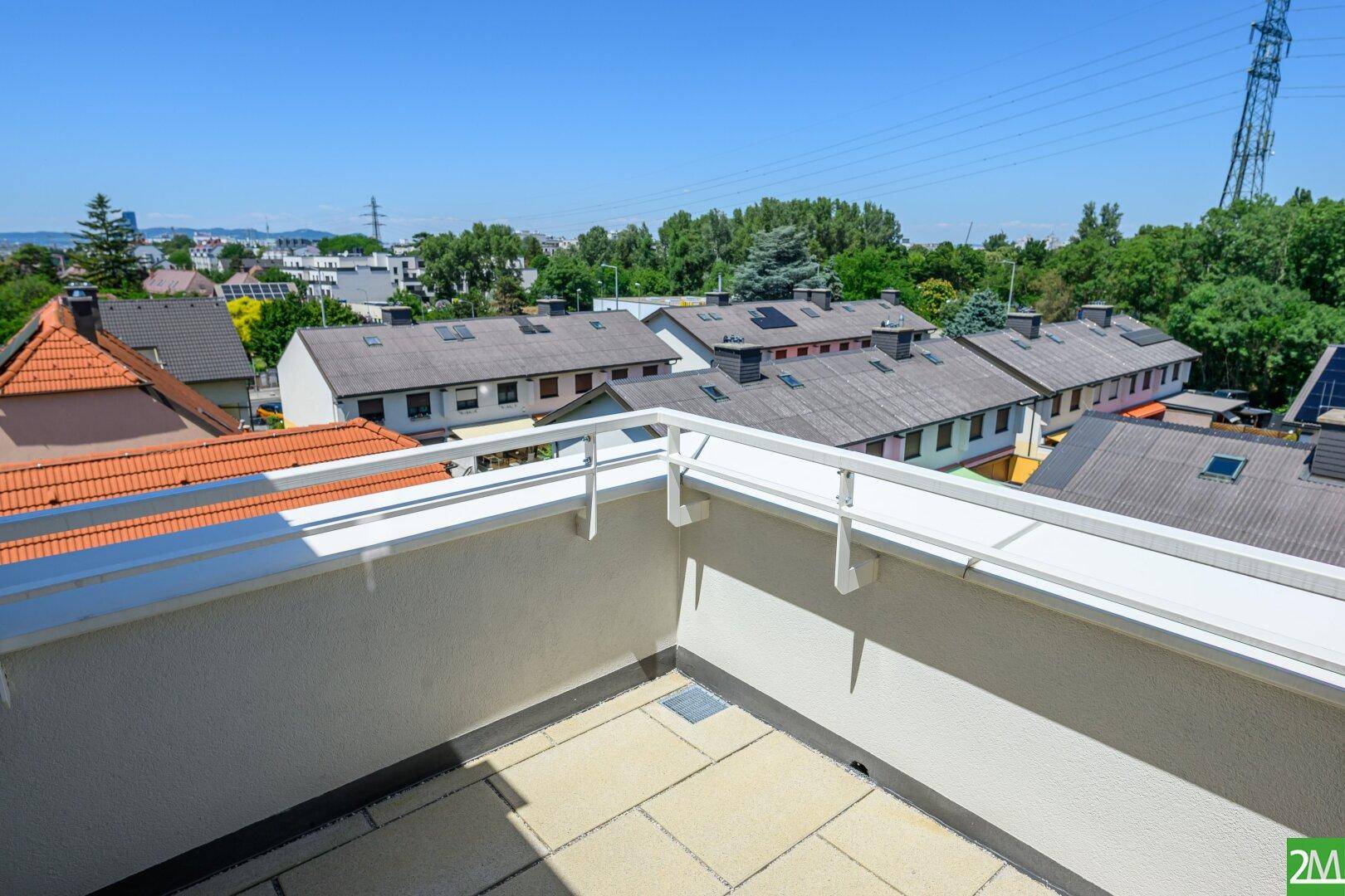 Geräumiger Balkon mit Fliesenboden und weitem Blick über die Dächer und die grüne Umgebung.