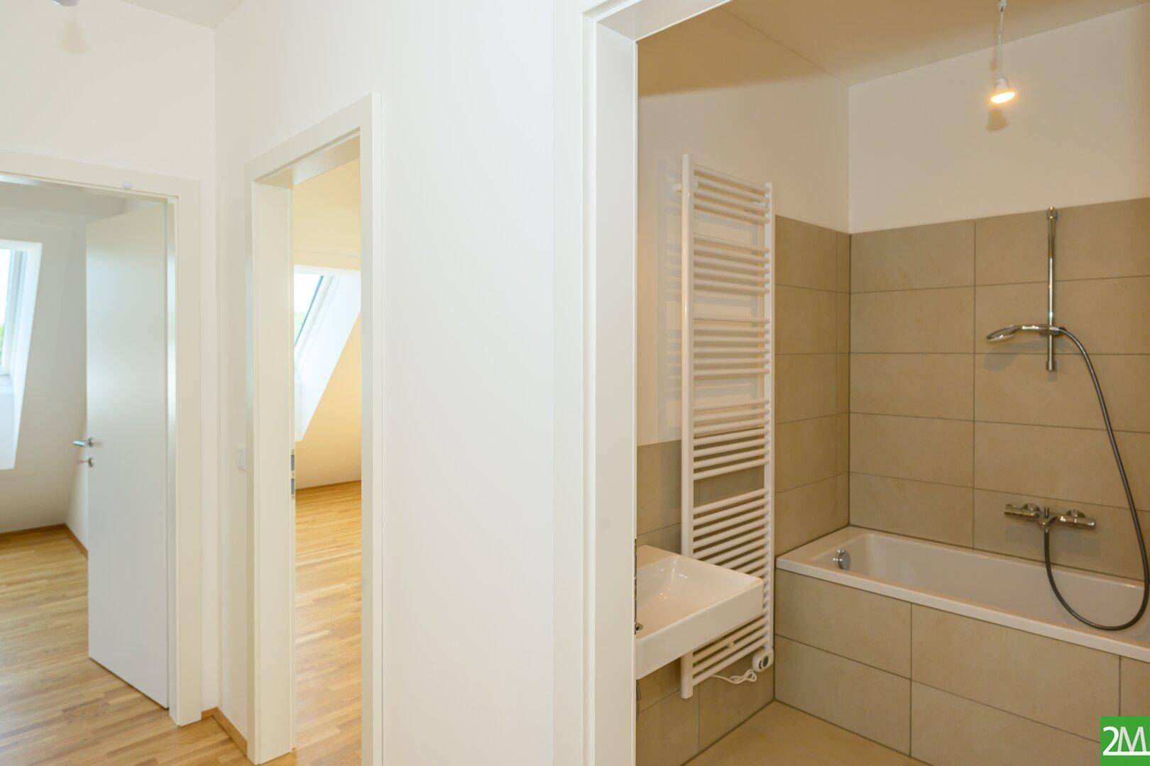Modernes Badezimmer mit beigefarbenen Fliesen, Badewanne und beheiztem Handtuchhalter.