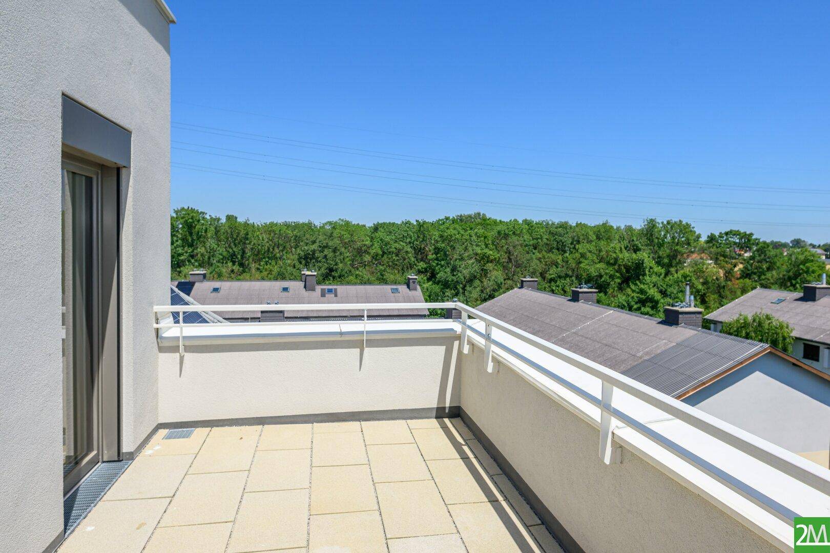 Geräumiger Balkon mit hellen Fliesen und Blick auf die grüne Umgebung und Dächer.