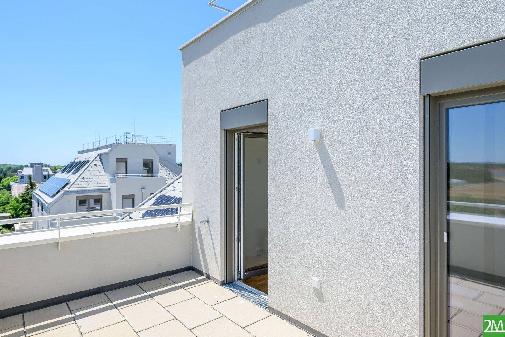 Heller Balkon mit Fliesenboden und Blick auf die umliegenden Dächer und die Stadt.