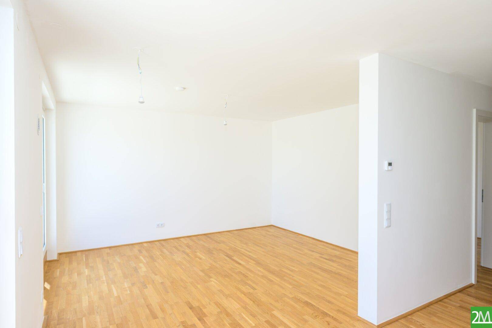 Geräumiger, unmöblierter Raum mit hellem Parkettboden und weißen Wänden, bereit zum Einzug.
