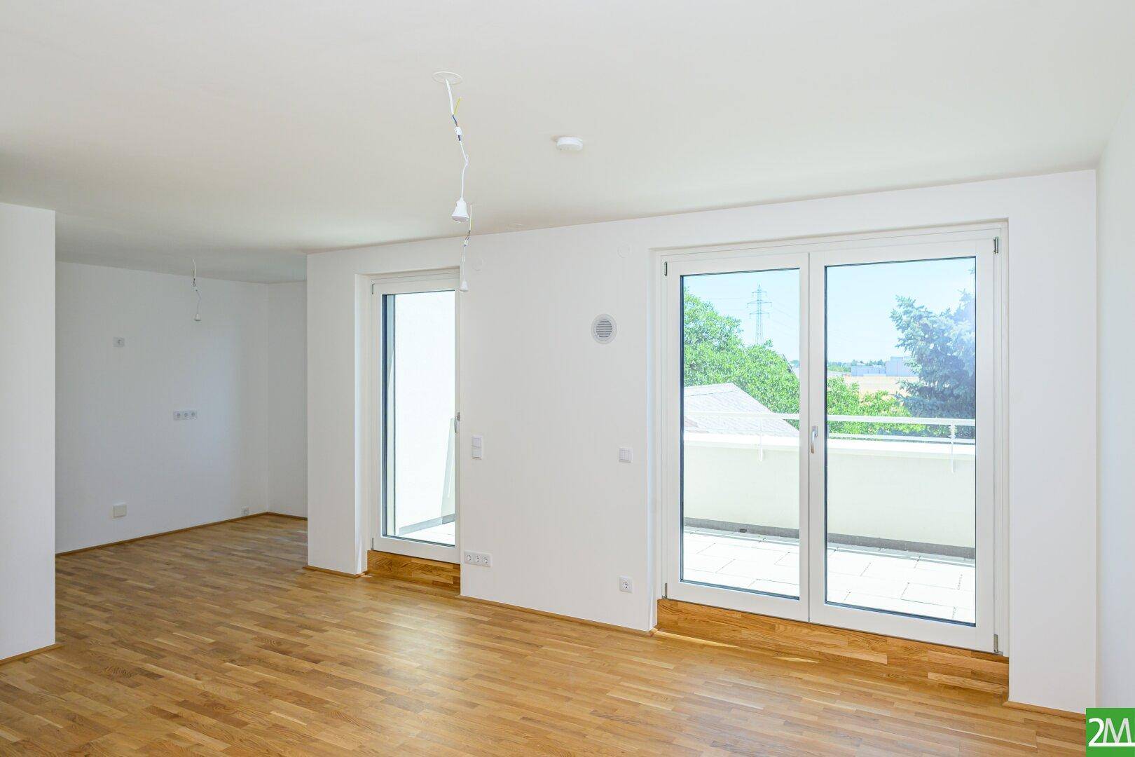 Geräumiger, heller Wohnbereich mit Eichenparkett und Zugang zu einem sonnigen Balkon.
