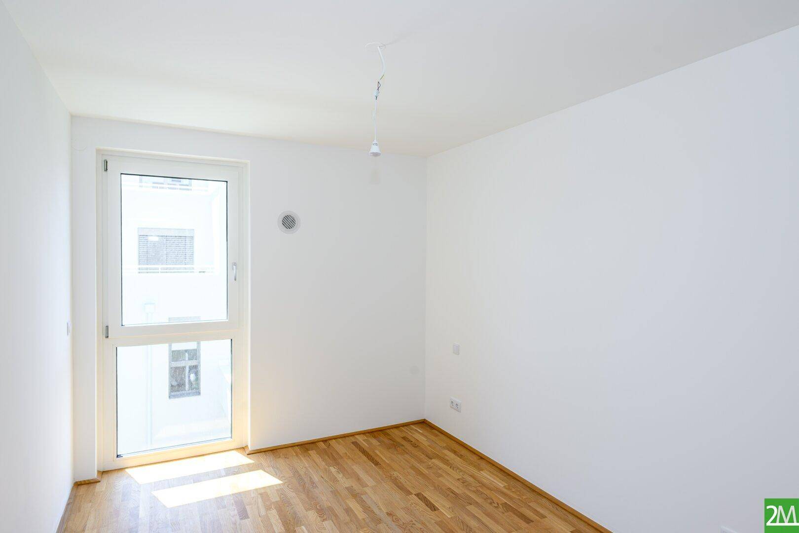 Helles Zimmer mit Parkettboden und Zugang zu einem französischen Balkon, ideal als Schlafzimmer.
