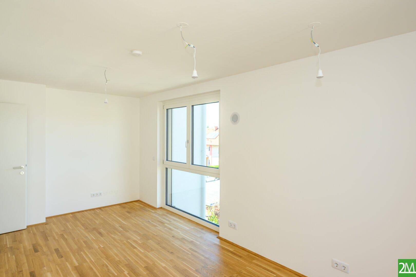 Leerer, heller Raum mit Holzboden und großem Fenster, bereit zum Einzug.
