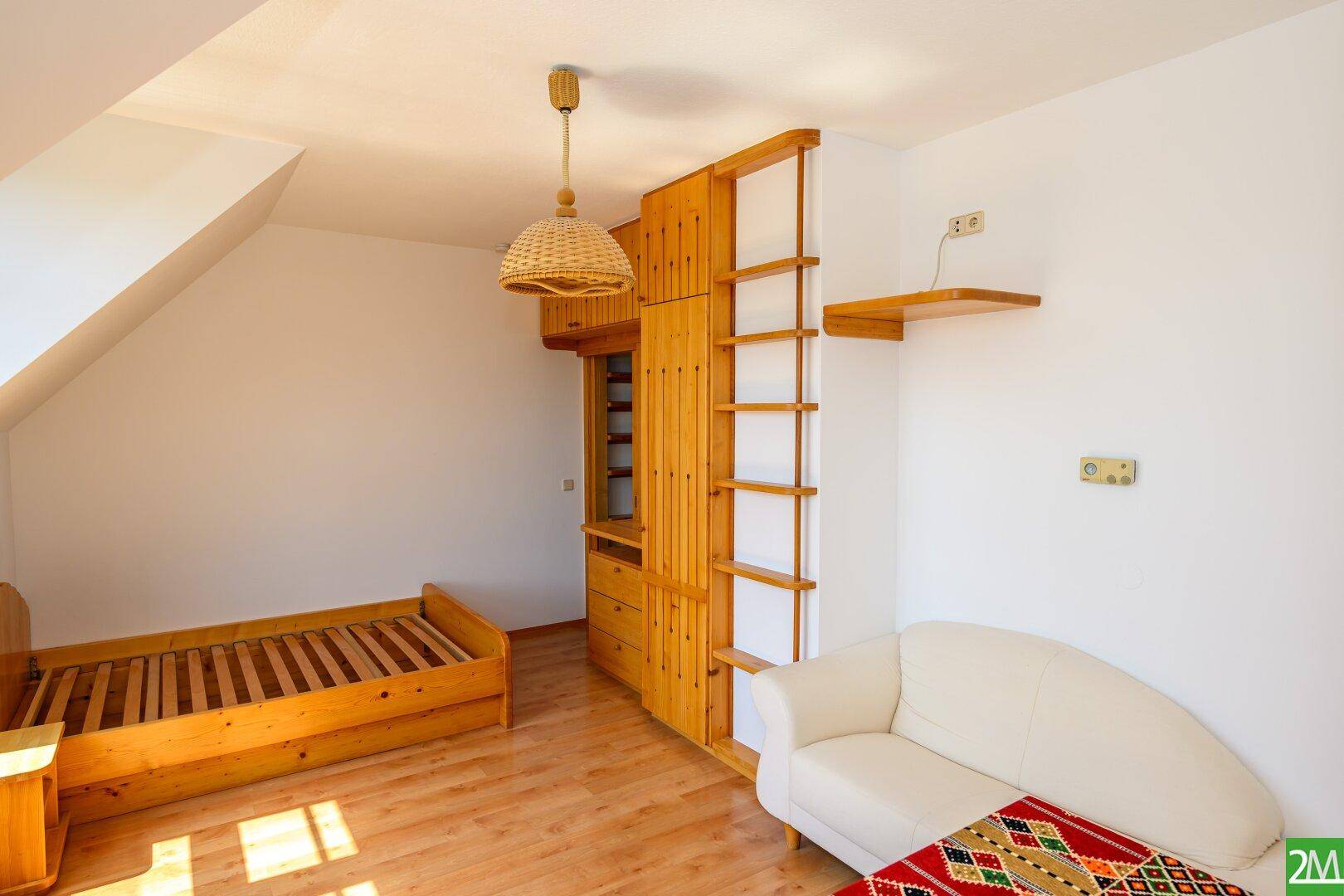 Schlafzimmer mit Holzboden, Dachschrägen und rustikalen Holzmöbeln, viel Tageslicht.