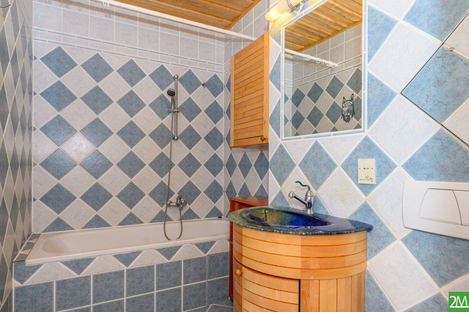 Badezimmer mit blauen und weißen Fliesen, Badewanne und Holzdecke im traditionellen Stil.