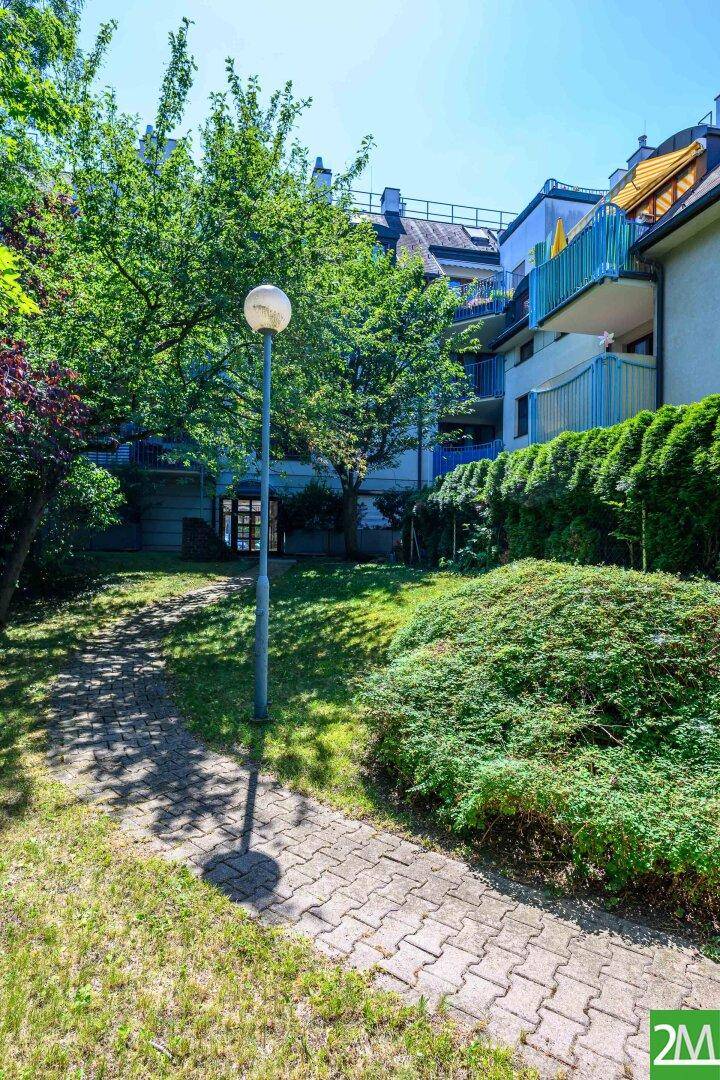 Außenansicht des Gebäudes mit gepflegtem Garten und Balkonen im Sonnenlicht.