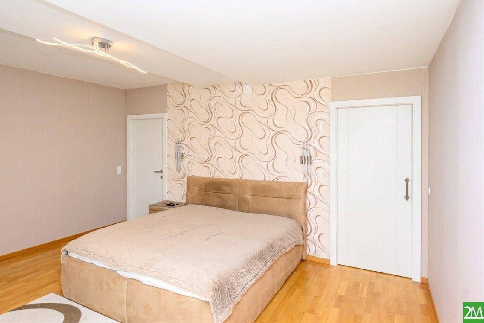 Gemütliches Schlafzimmer mit Doppelbett, Parkettboden und dekorativer Tapete.
