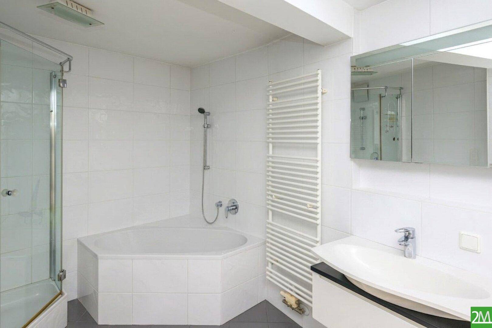 Helles Badezimmer mit Badewanne, Duschkabine, Waschbecken und beheiztem Handtuchhalter.