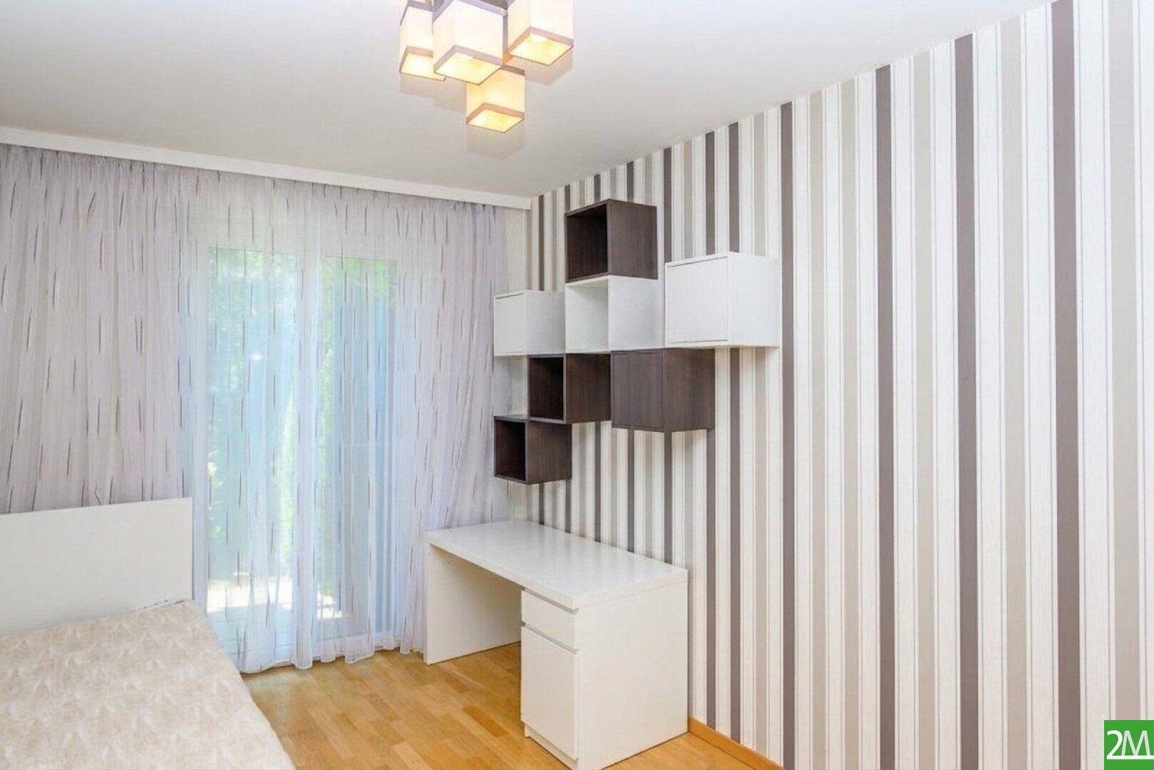 Helles Zimmer mit Schreibtisch, Regalen und gestreifter Tapete, ideal als Kinder- oder Arbeitszimmer.
