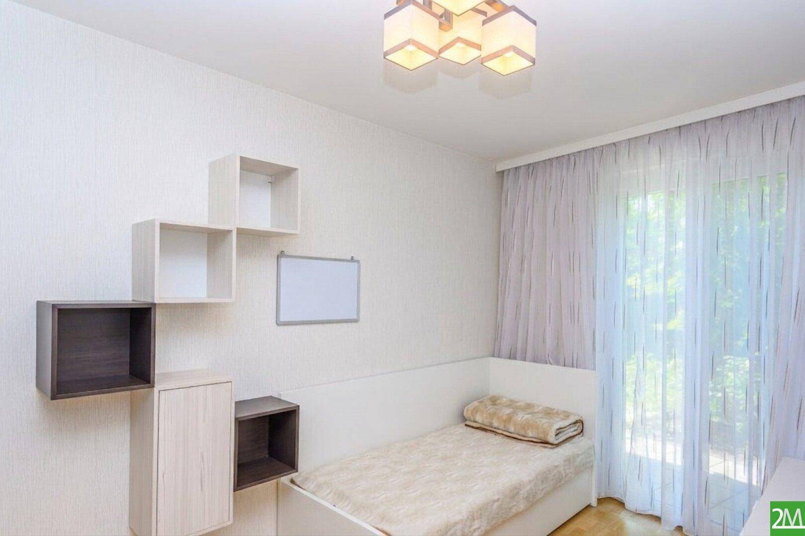 Freundliches Schlafzimmer mit Einzelbett, Regalen und viel Tageslicht durch das Fenster.