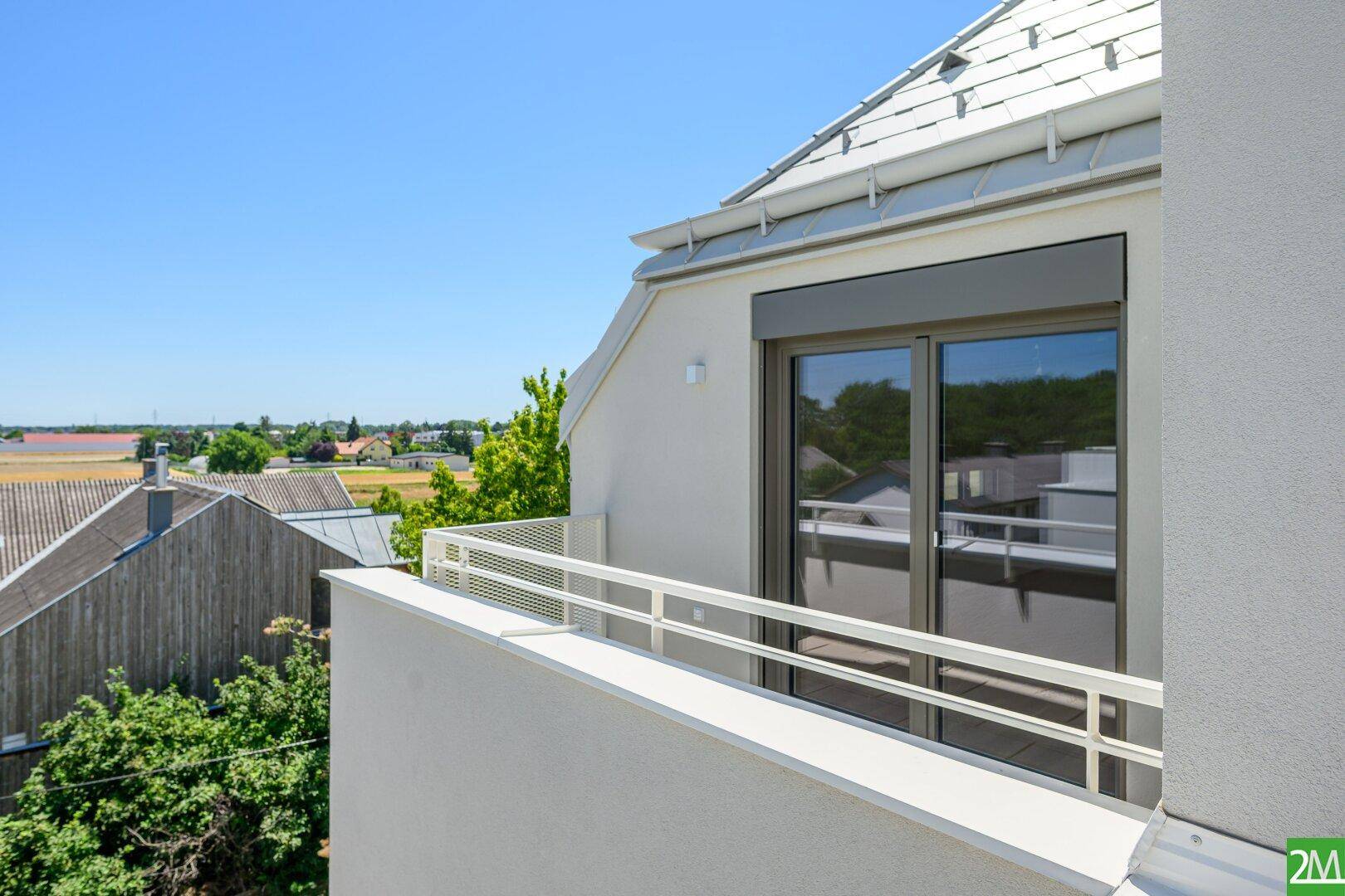 Balkon mit Blick auf die Umgebung und großer Glasfront mit Rollladen.