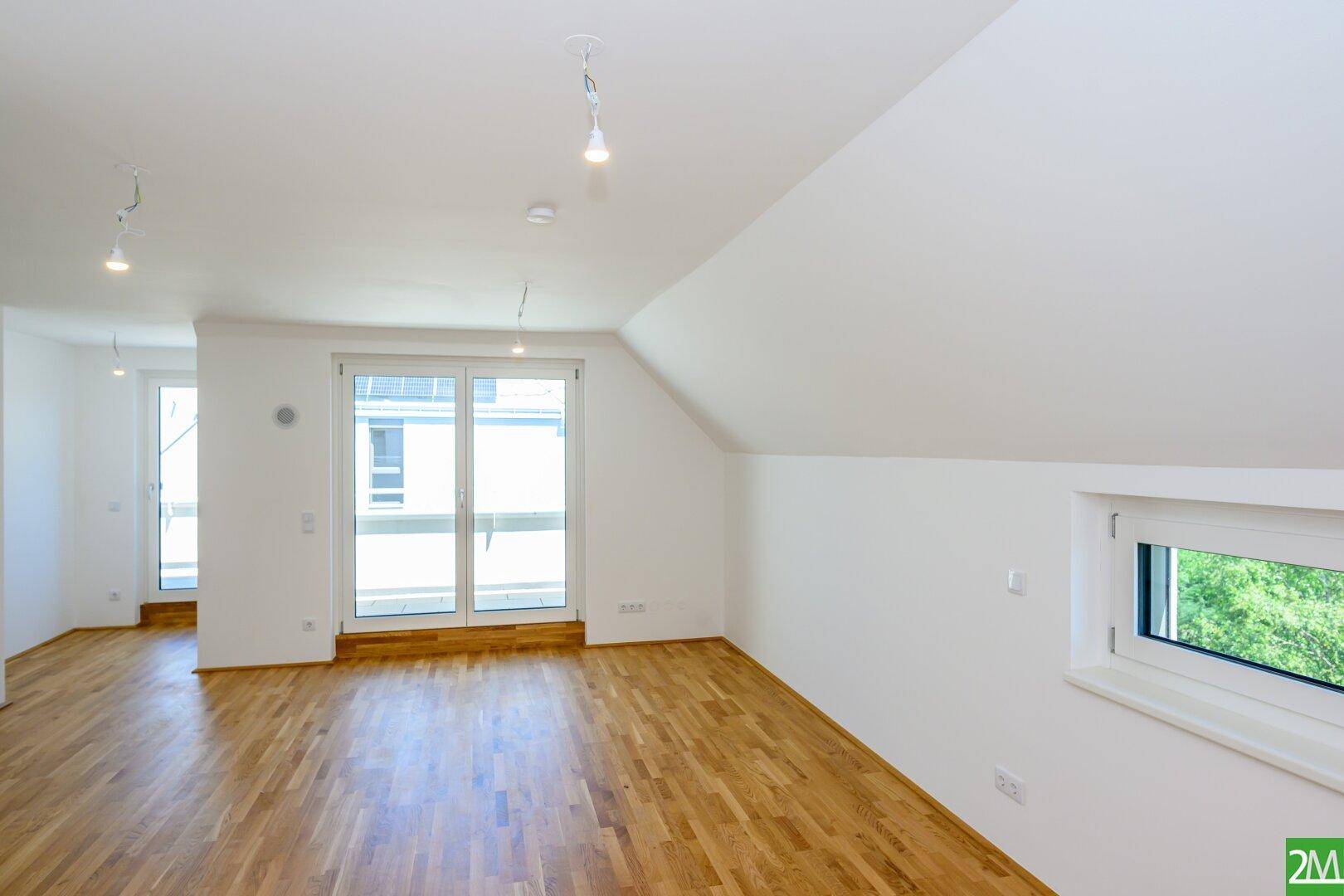 Heller, leerer Raum mit Holzboden, Dachschräge und großem Fenster mit Zugang nach draußen.