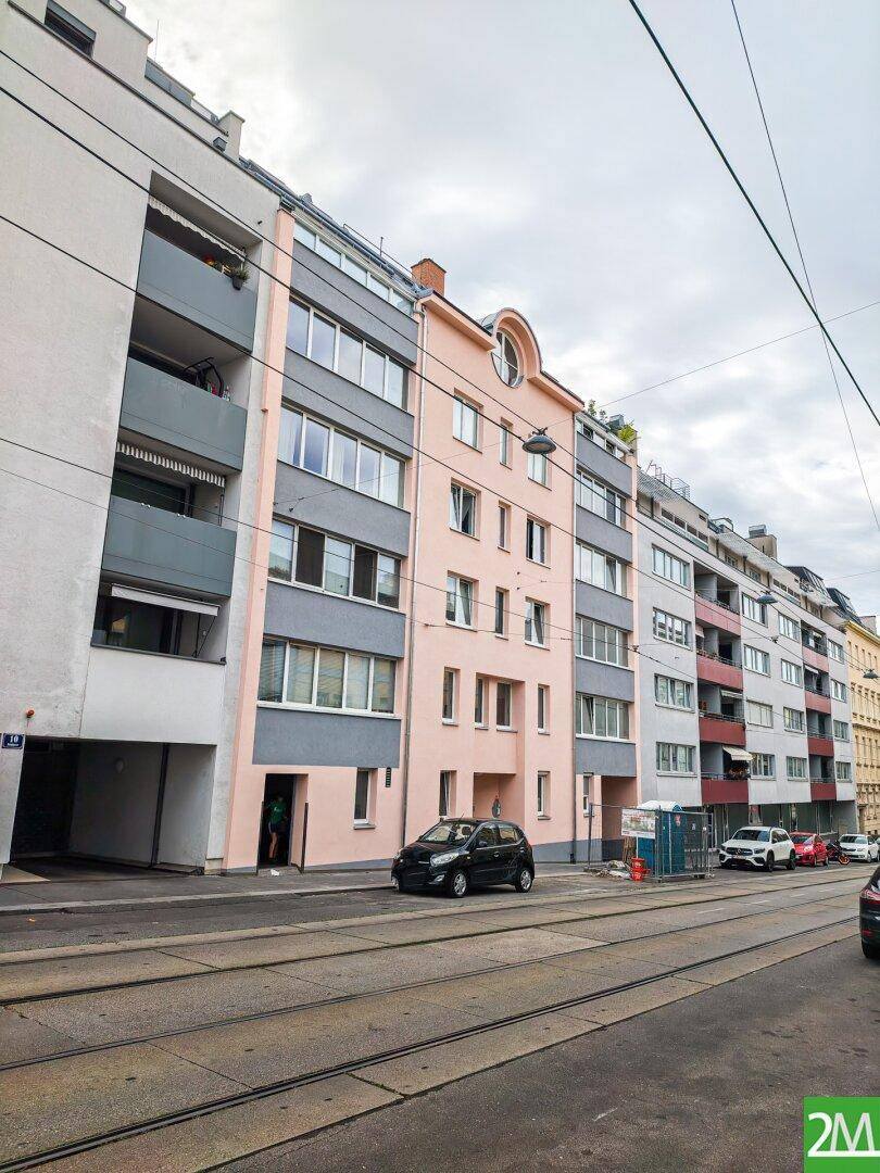 Ansicht einer städtischen Straße mit Gebäuden und einer Straßenbahnlinie unter bewölktem Himmel.